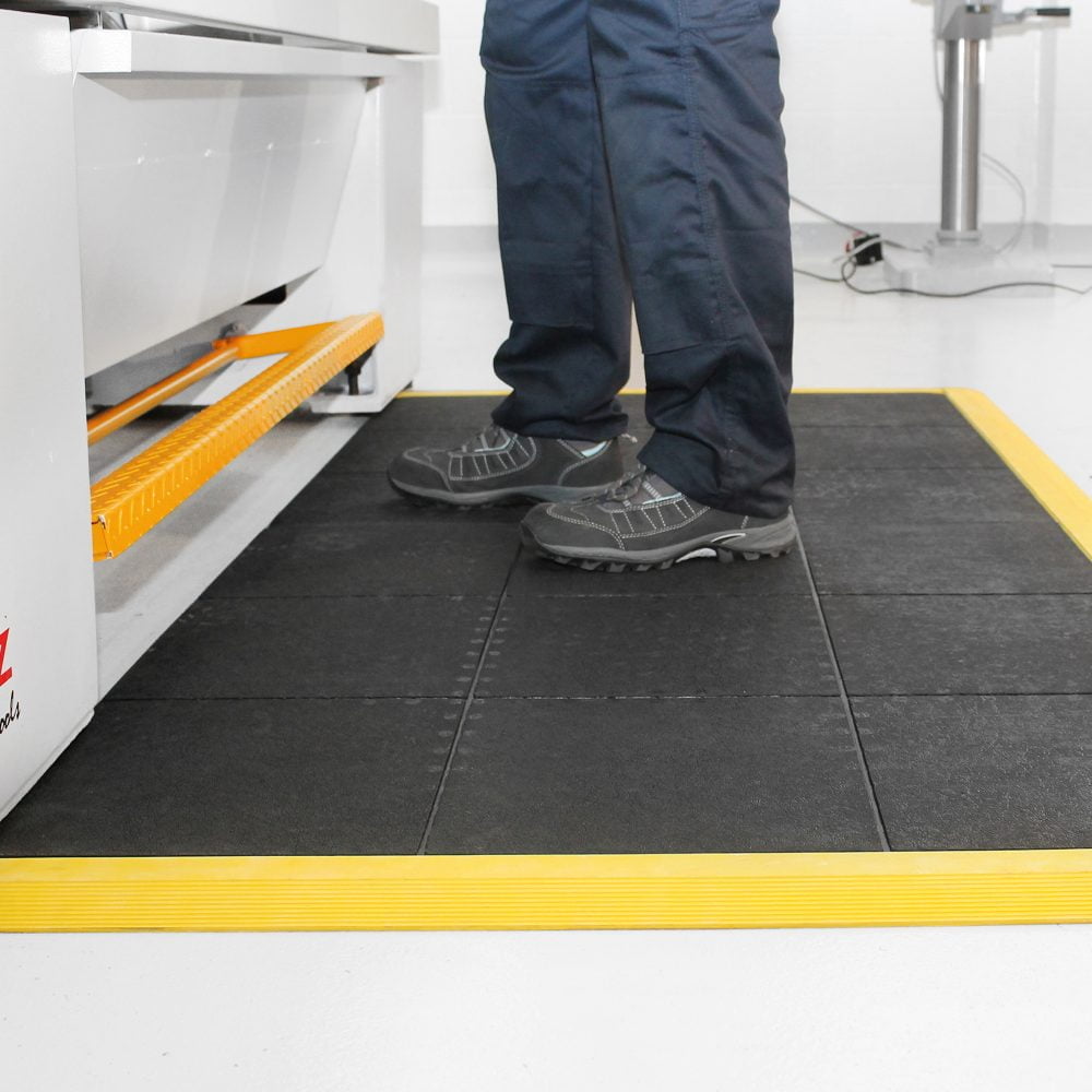 Person-standing-beside-a-workstation- on-a-black/yellow-solid-fatigue-step- mat